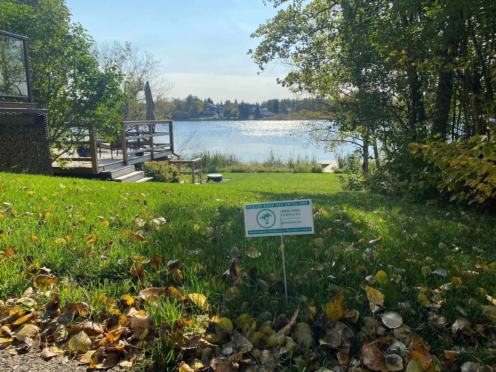 Green Oasis treatment sign at lakeside property in autumn